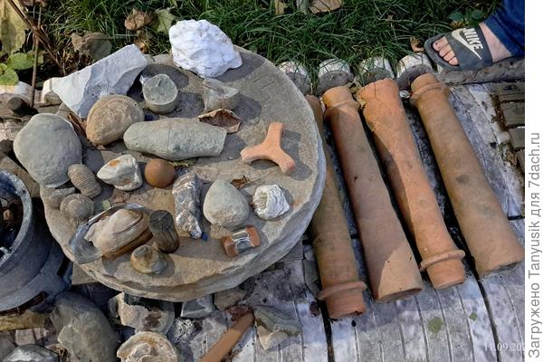 На жерновах лежат древние окаменелости, справа - трубы водопровода.
